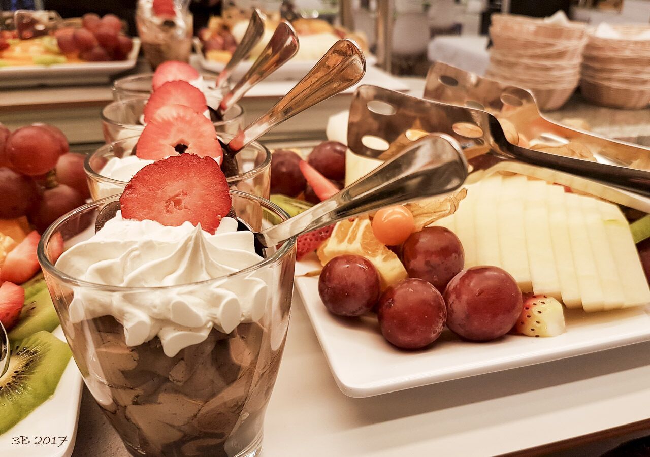 Una bandeja de postres con crema batida, chocolate y fresas, junto a un plato de uvas y queso.
