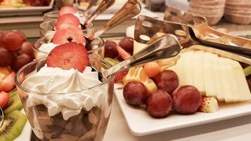 Una bandeja de postres con crema batida, chocolate y fresas, junto a un plato de uvas y queso.