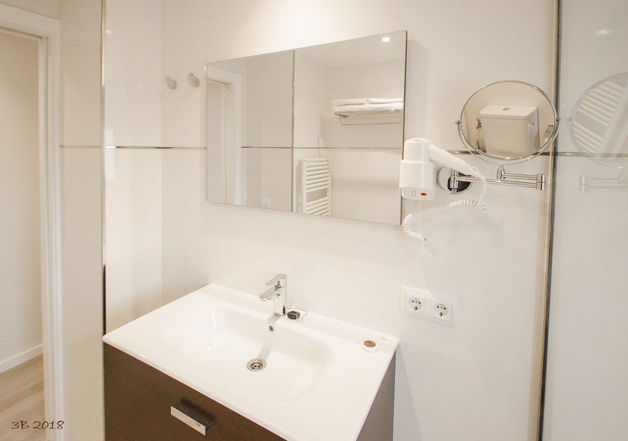 Un baño moderno con un lavamanos blanco, un espejo y un perchero para toallas.