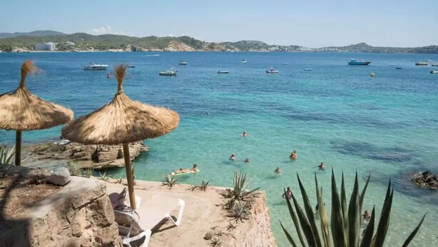 Una playa con agua turquesa cristalina, sombrillas y tumbonas.