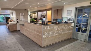 A reception desk with a wooden finish and a sign in French. - Kyriad Cambrai (Fontaine-Notre-Dame)