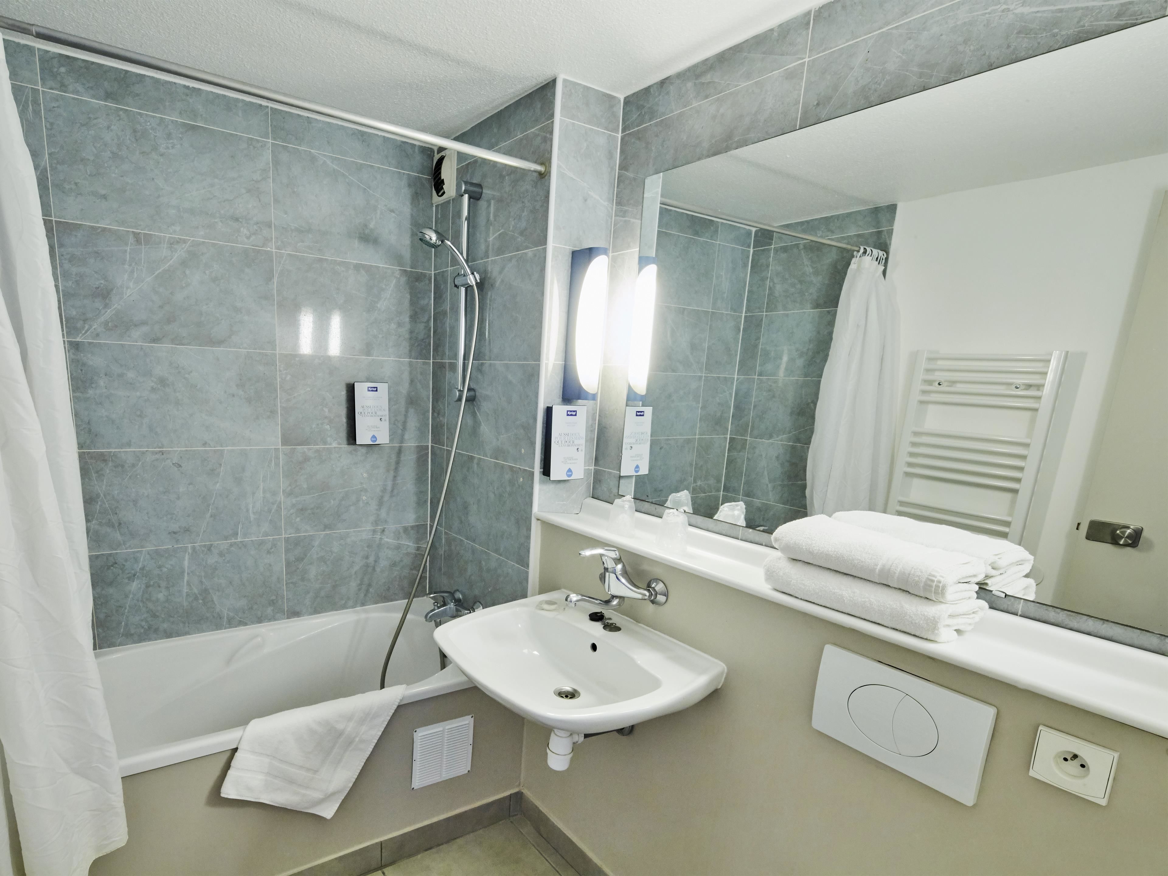 Une salle de bain moderne équipée d’une baignoire, d’un lavabo, d’un miroir et d’un porte-serviettes.