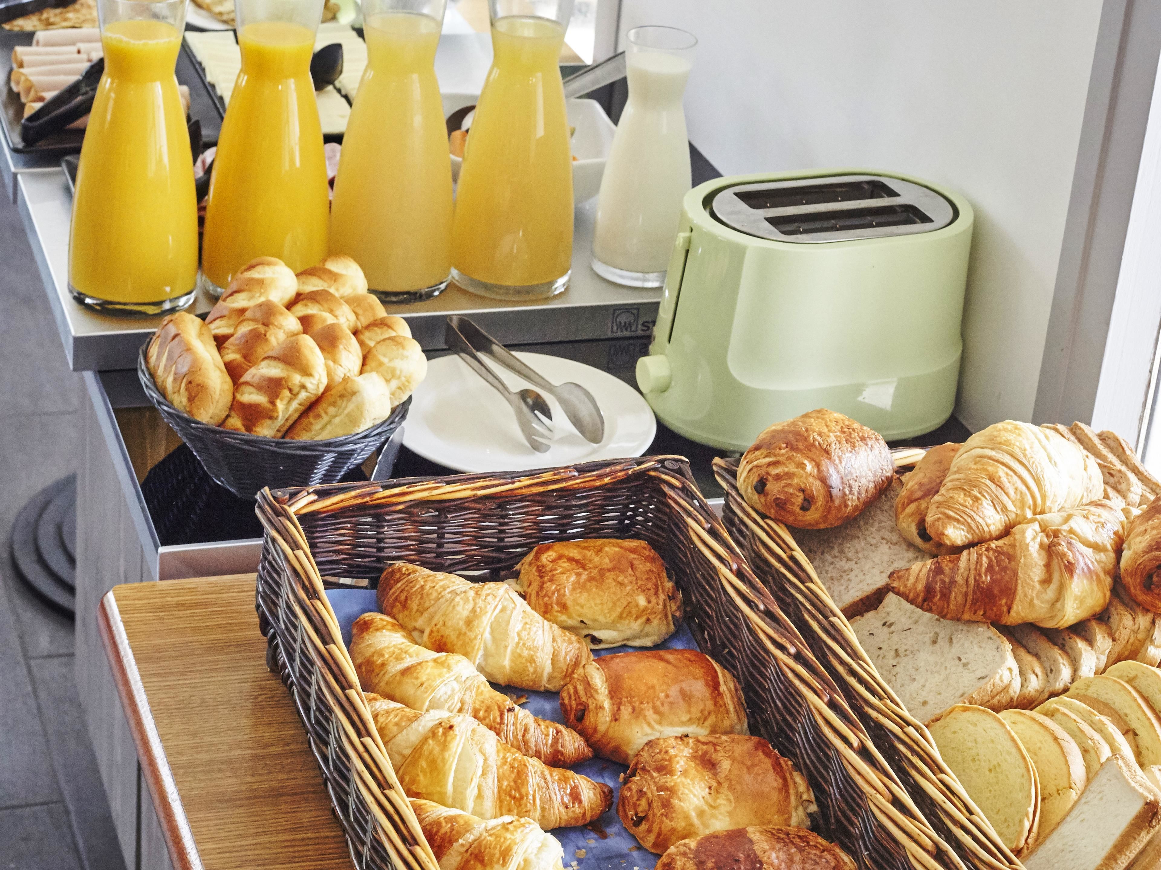 En frukostbuffé med croissanter, bröd, juice och en brödrost.