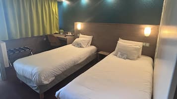 A hotel room with two single beds, a desk, and a chair.