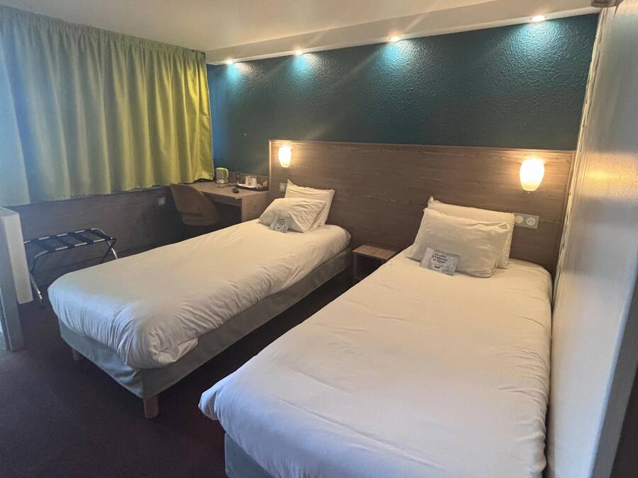 A hotel room with two single beds, a desk, and a chair.