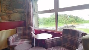 A cozy room with plaid furniture, a stone wall, and a large window with a view of greenery. - Ratagan Youth Hostel (Kyle)