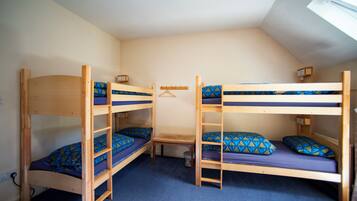 A room with two bunk beds, a small table, and a wall-mounted shelf.