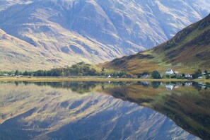 A serene lake with a reflection of the surrounding hills and a small house on the shore. - Ratagan Youth Hostel (Kyle)