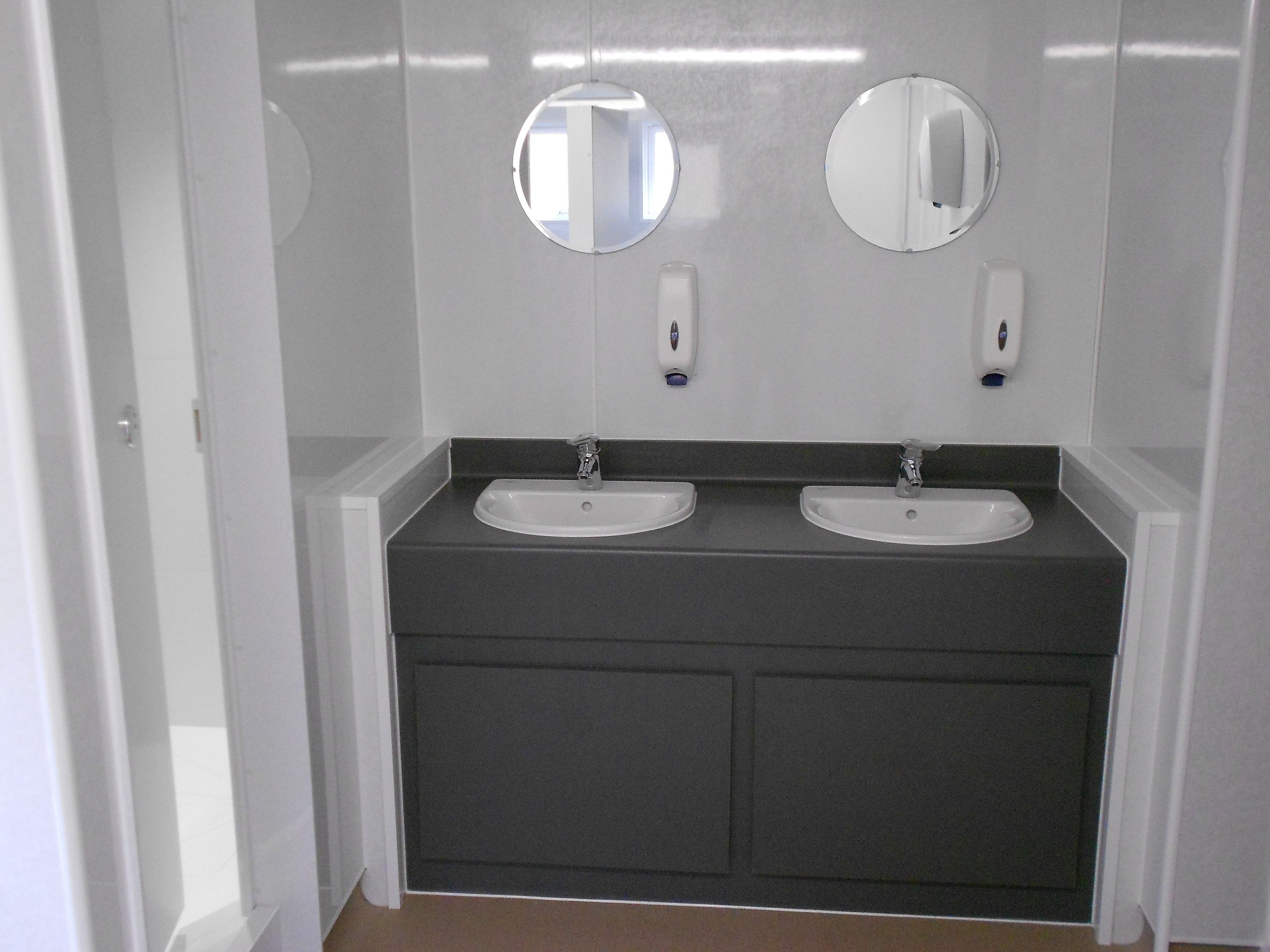A bathroom with two sinks, two mirrors, and soap dispensers.