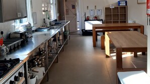 A kitchen with stainless steel appliances, a long counter, and wooden tables. - Glenbrittle Youth Hostel (Minginish)