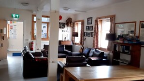 A spacious living area with a wooden table, leather sofas, and a bookshelf. - Glenbrittle Youth Hostel (Minginish)