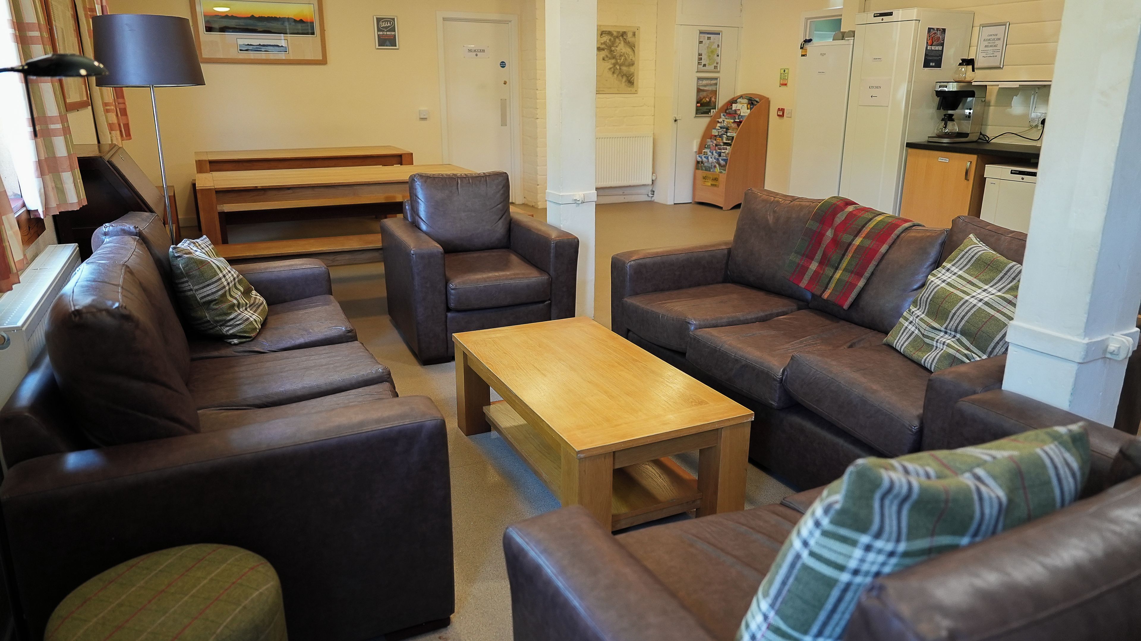 Ein gemütliches Wohnzimmer mit Ledersofas, einem Holztisch und einer Küchenzeile mit Geräten.