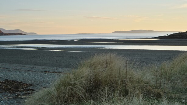 A coastal landscape with a beach, grassy dunes, and distant mountains under a clear sky. - Glenbrittle Youth Hostel (Minginish)