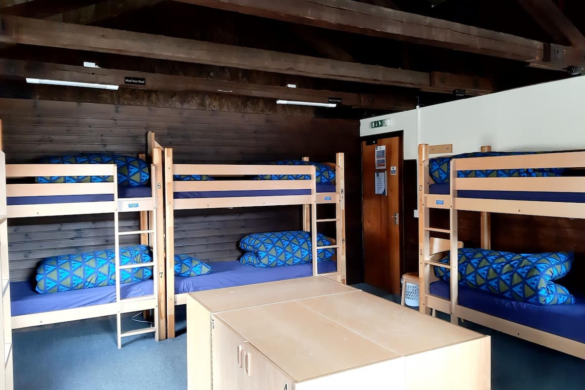 A dormitory room with bunk beds, a wooden table, and a door with a sign.