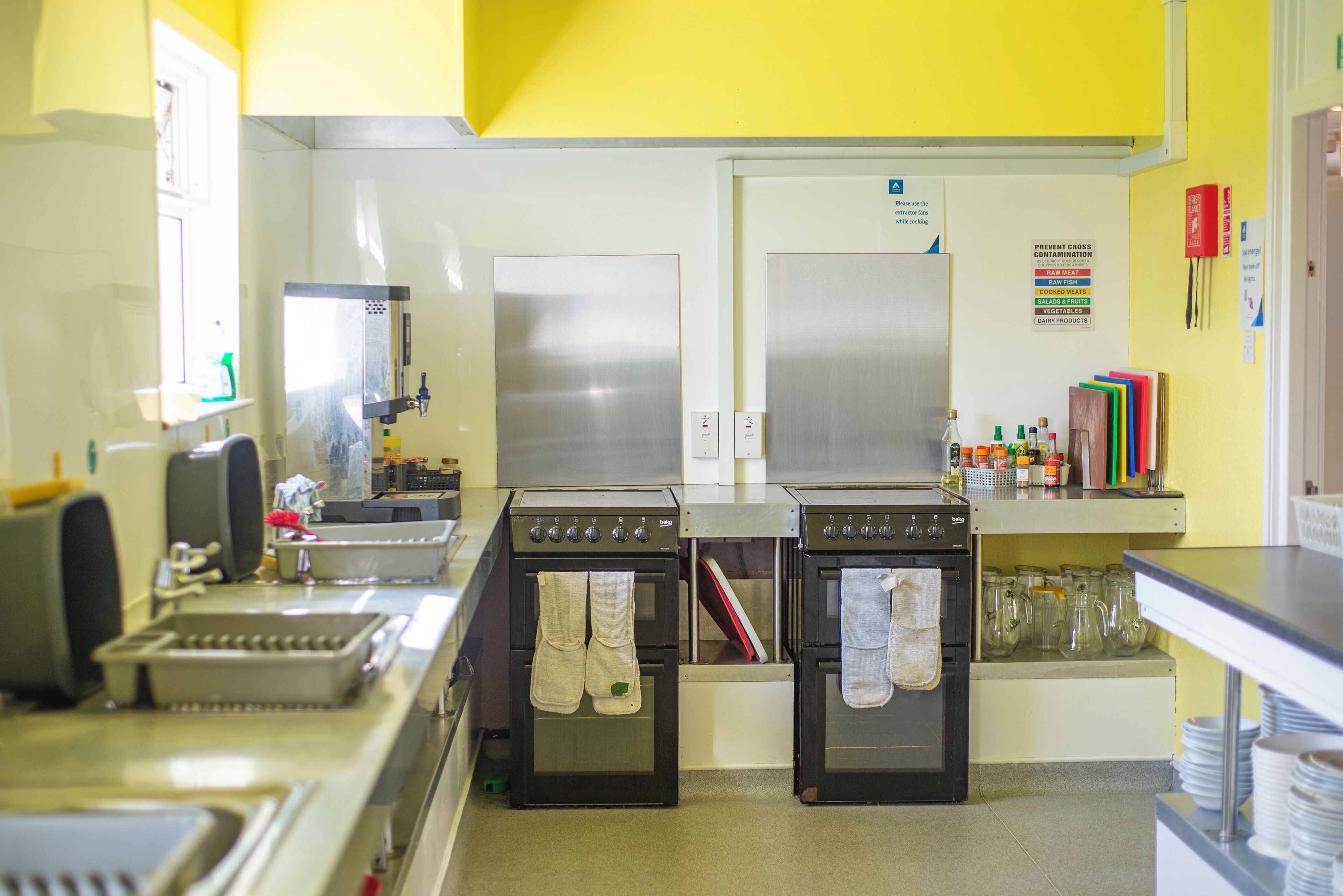 A kitchen with two ovens, a sink, and a window. There are various kitchen utensils and appliances visible.