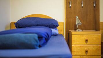 A bed with blue bedding, a wooden nightstand with drawers, and a lamp.