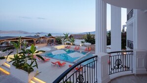 A pool area with lounge chairs and umbrellas, surrounded by white columns and a view of the landscape. - Vila Kalcuni (Sarandë)