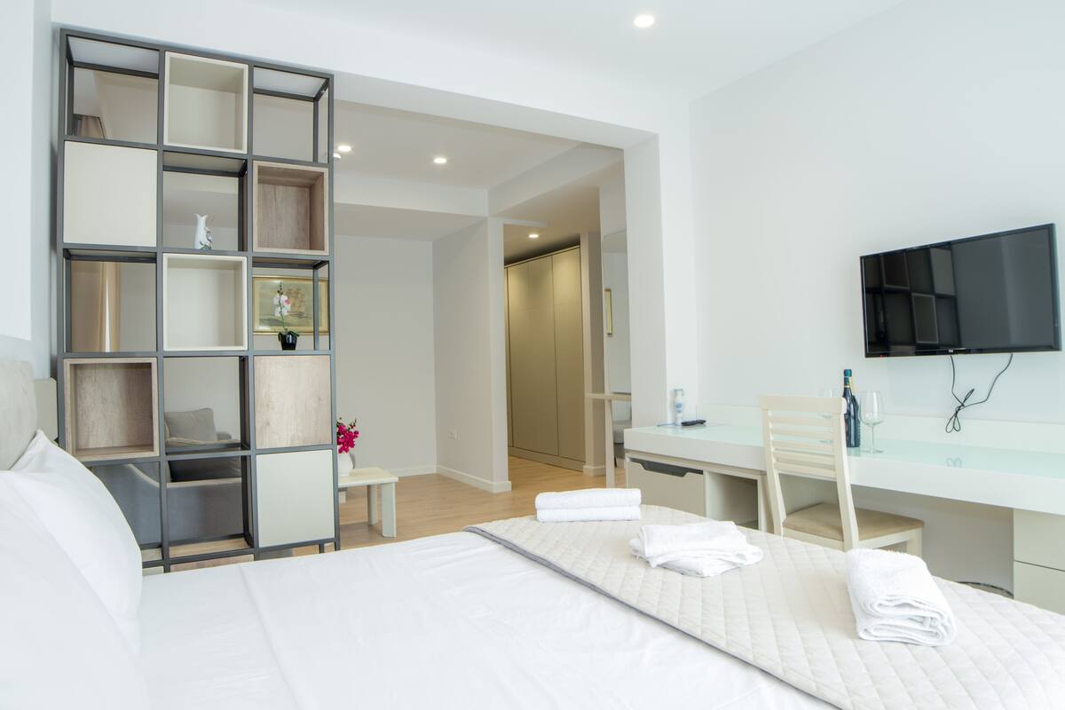 Quarto de hotel moderno com cama, escrivaninha, cadeira, televisão e guarda-roupa.