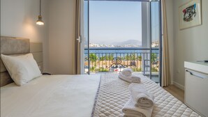 A hotel room with a bed, a desk, and a view of the sea and cityscape. - Vila Kalcuni (Sarandë)