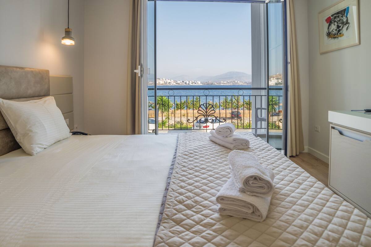 Quarto de hotel com cama, escrivaninha e vista para o mar e para a cidade.