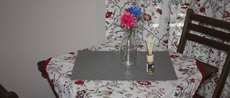 A dining table with a floral tablecloth, a vase with flowers, and a candle holder.