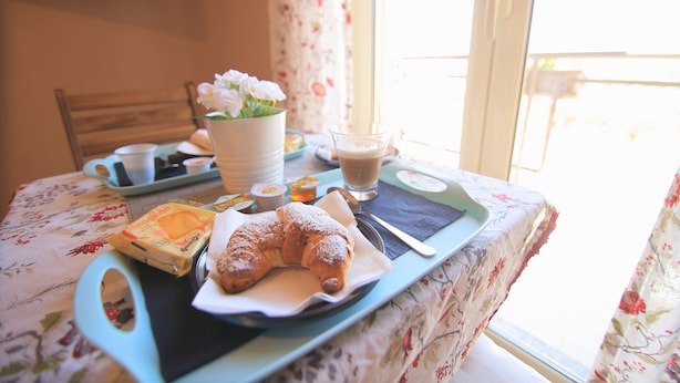 Un safata de petit esmorzar amb croissant, cafè i flors sobre una taula amb estovell floral.