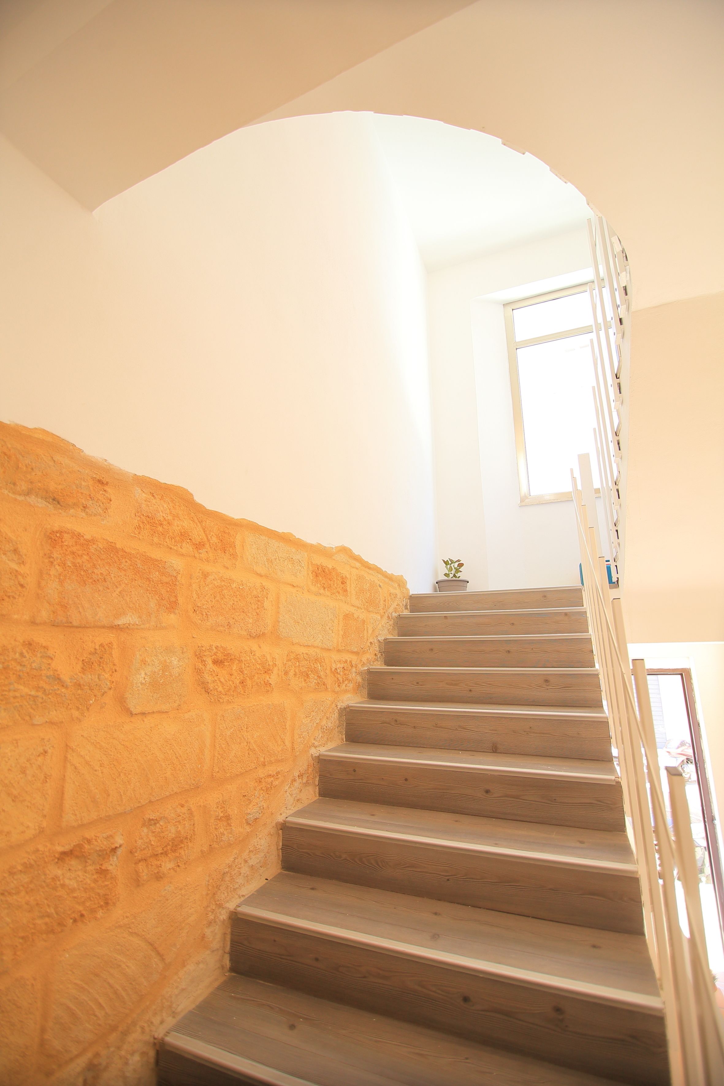Eine Treppe mit Holzdielen und einer Steinwand, die zu einem Raum mit Fenster und einer kleinen Pflanze führt.