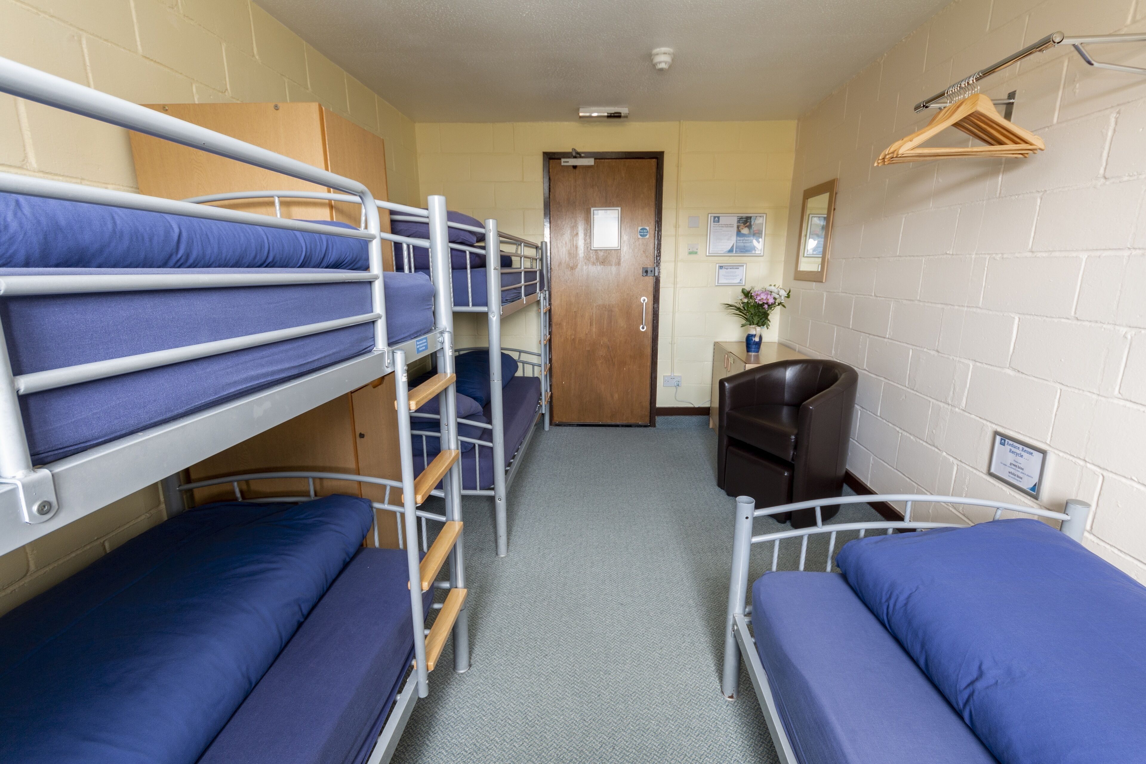 A dormitory room with bunk beds, a desk, and a chair.