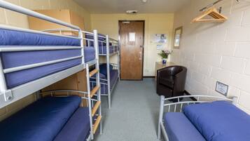 A dormitory room with bunk beds, a desk, and a chair.