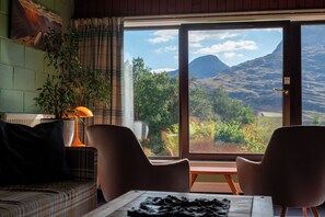 A room with a view of mountains, a sofa, two chairs, a table, and a lamp. - Torridon Youth Hostel (Achnasheen)