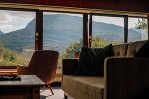 A room with a large window offering a view of mountains. There is a sofa and a chair inside. - Torridon Youth Hostel (Achnasheen)
