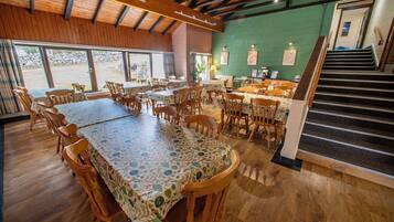 Un restaurante con mesas y sillas de madera, una pared verde y una escalera que sube a un nivel superior.