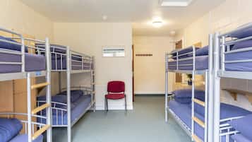 A dormitory room with bunk beds, a red chair, and a radiator.