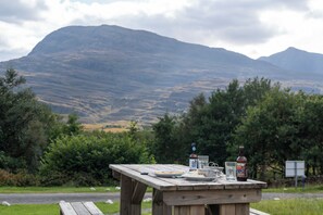 A picnic table with plates, glasses, and bottles in a natural setting with mountains in the background. - Torridon Youth Hostel (Achnasheen)