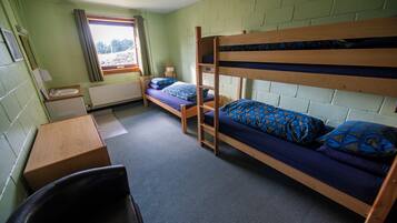 Ein Schlafsaalzimmer mit Etagenbetten, einem Schreibtisch, einem Stuhl und einem Fenster mit Vorhängen.