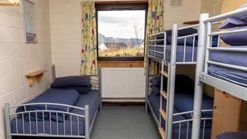 Una habitación de residencia estudiantil con literas, una ventana con cortinas, un mapa en la pared y un radiador.