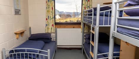 Una habitación de residencia estudiantil con literas, una ventana con cortinas, un mapa en la pared y un radiador.
