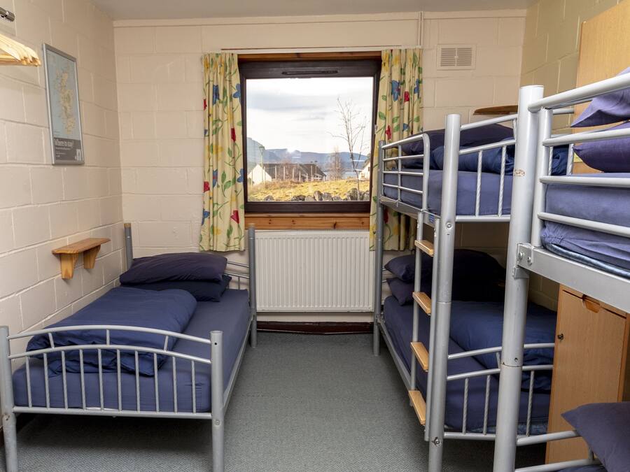 A dormitory room with bunk beds, a window with curtains, a map on the wall, and a radiator.