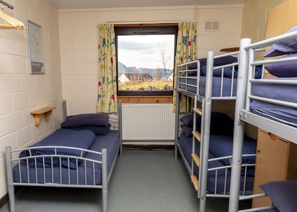 A dormitory room with bunk beds, a window with curtains, a map on the wall, and a radiator. - Torridon Youth Hostel (Achnasheen)