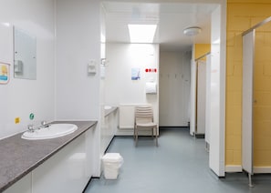 A clean, modern bathroom with a sink, mirror, and toilet. There is a chair and a trash bin. - Torridon Youth Hostel (Achnasheen)