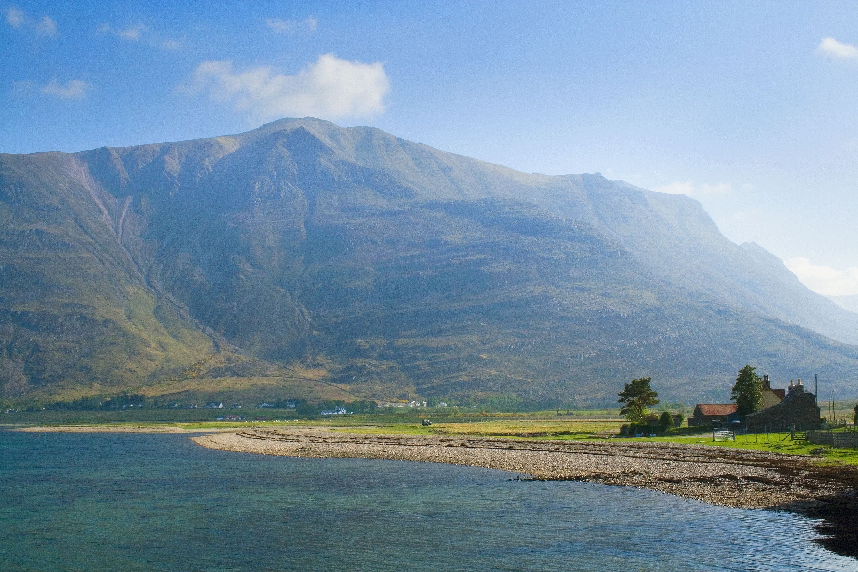 A coastal landscape with a mountain in the background, a small settlement, and a clear sky.