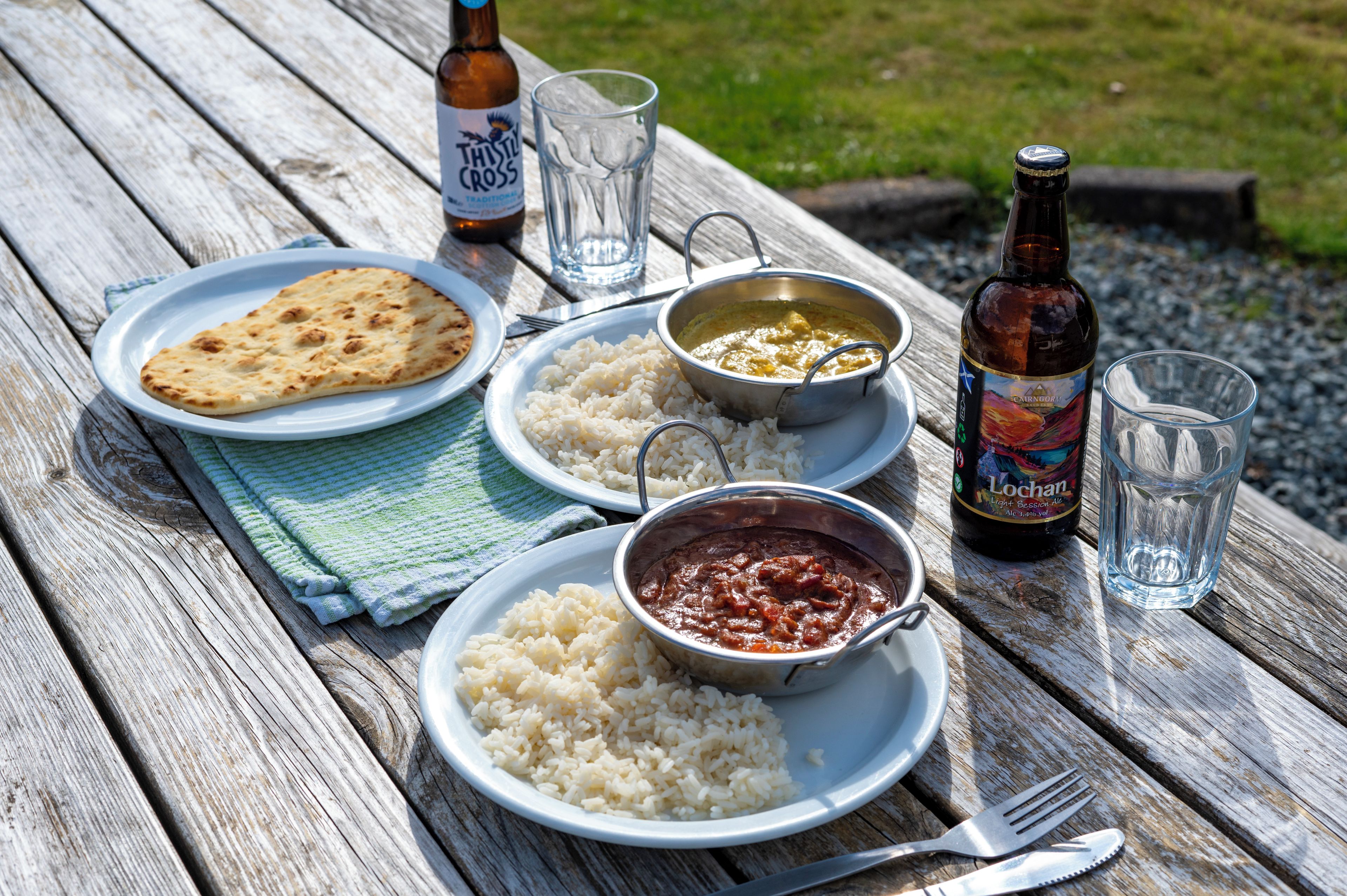 A picnic setup on a wooden table with plates of food, a bottle of beer, and a glass.