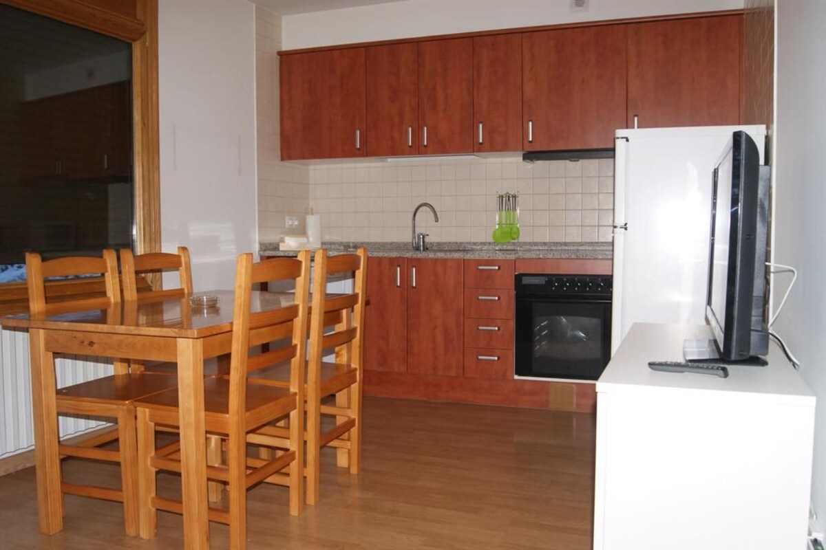 A kitchen with wooden cabinets, a dining table with chairs, a refrigerator, and a microwave.