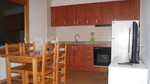 Een keuken met houten kastjes, een eettafel met stoelen, een koelkast en een fornuis.