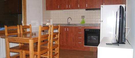 A kitchen with wooden cabinets, a dining table with chairs, a refrigerator, and a stove.