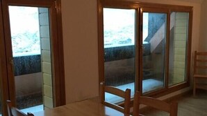 Een eetruimte met een houten tafel en stoelen, grote ramen en uitzicht op een gebouw.