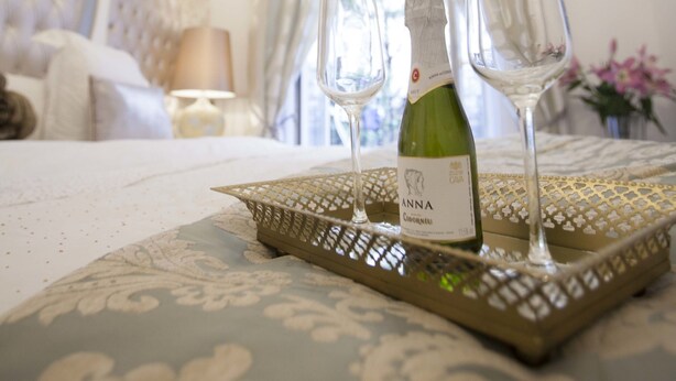 A neatly arranged bedroom with a bed, a bedside table, a chandelier, and a tray with a bottle and glasses. - Hostal Boutique Palace - Adults Only (Madrid)