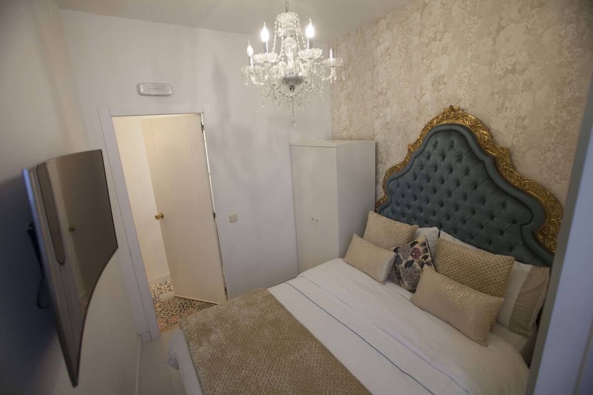 Ein Schlafzimmer mit einem gepolsterten Kopfteil, einer Chandelierleuchtre und einem Bett mit vielen Kissen.
