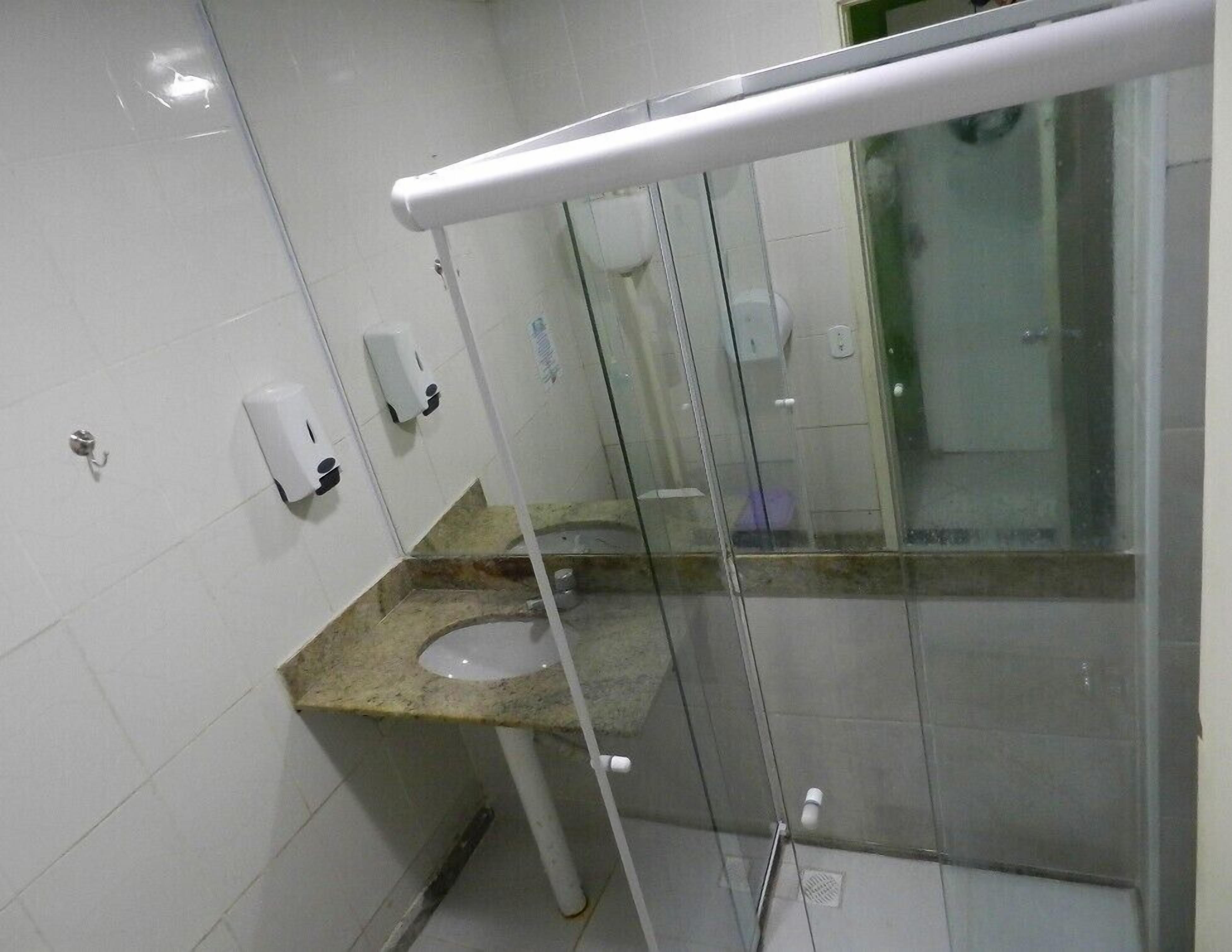 A modern bathroom with a glass partition, a marble sink, and a hand soap dispenser.