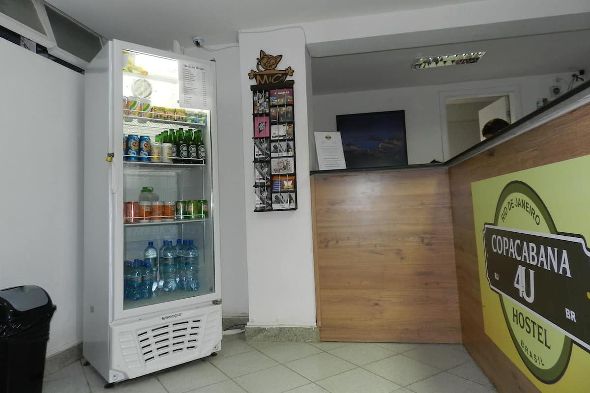 A hotel reception area with a refrigerator stocked with beverages, a wooden reception desk, and a wall-mounted menu board.